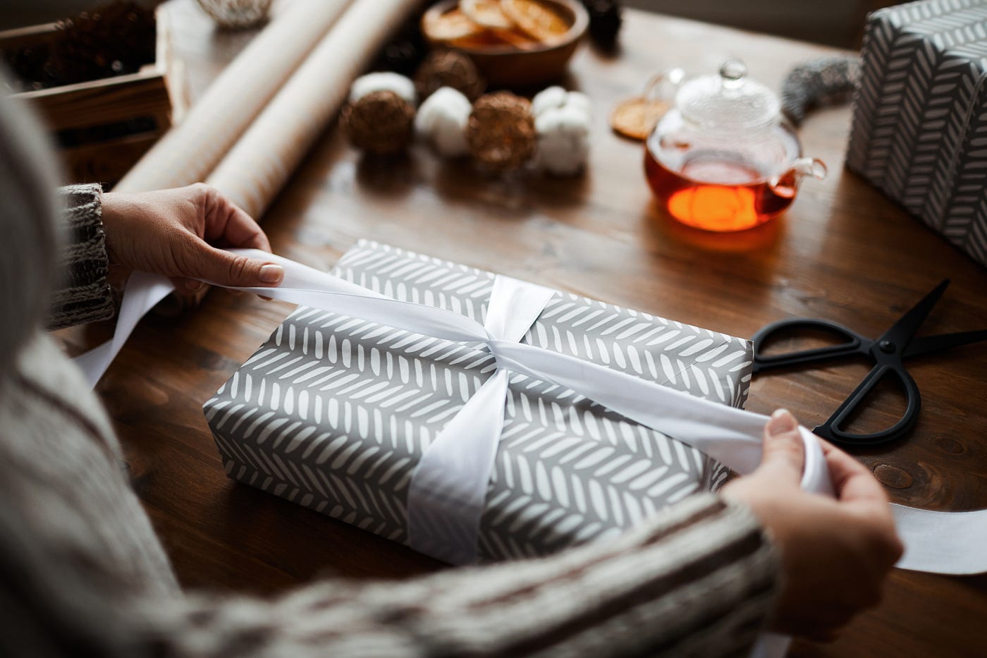 Close-up of woman sitting at the table and decorating gift box with ribbon for Christmas.