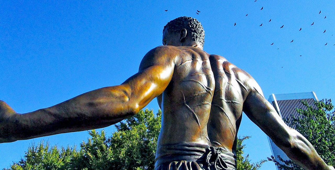Bronze statue of an African-American man, shirtless with whip scars on his back