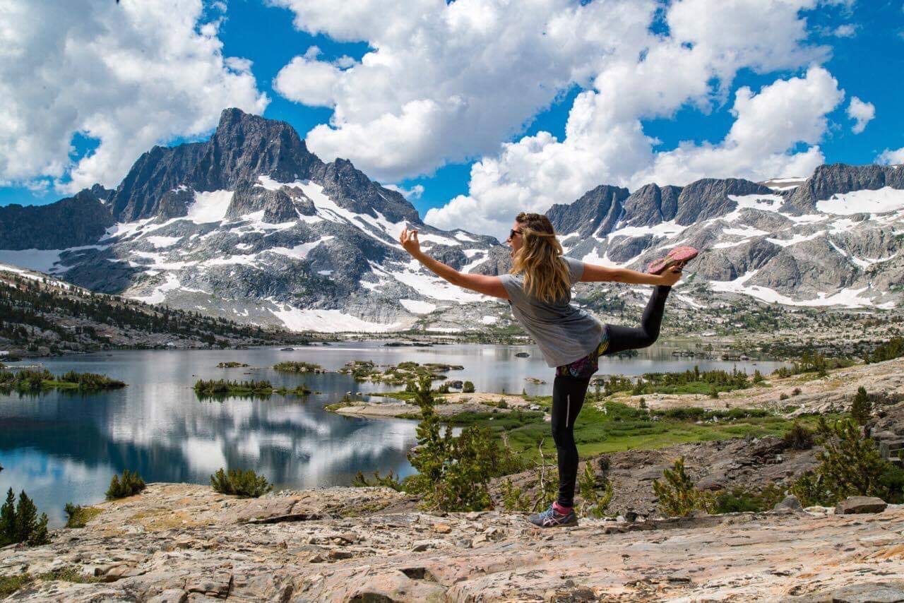 woman doing a yoga pose in front of a lake and mountains