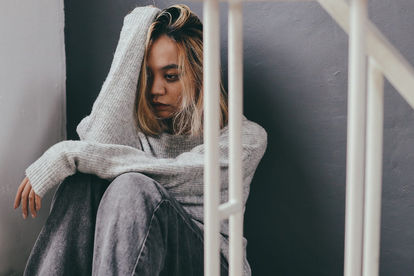 A dishevelled young woman sits in a stair with her knees folded up and an arm resting against her head.