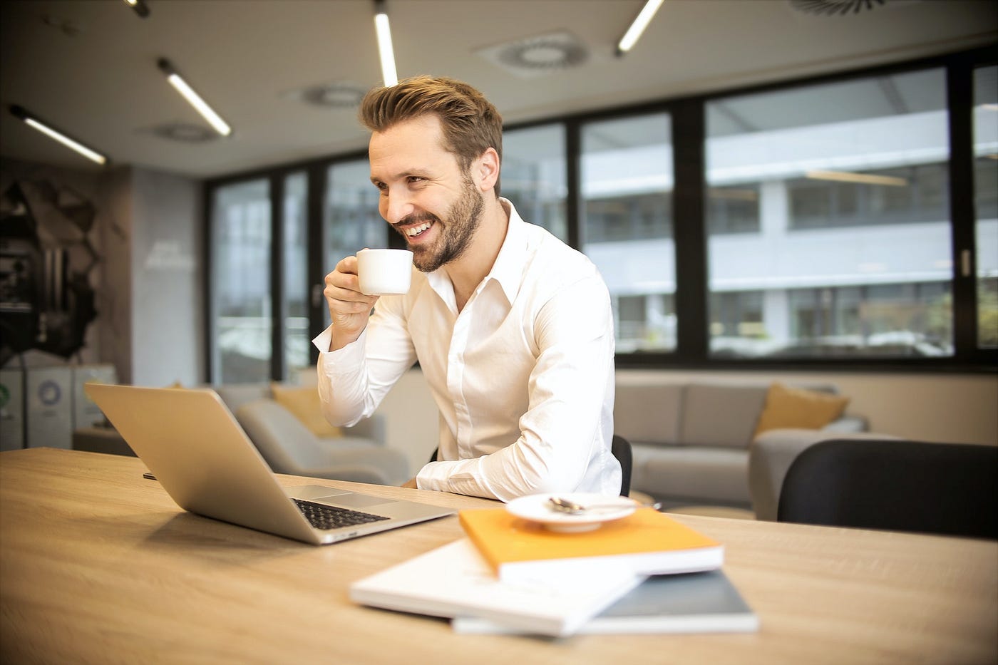 man in front of a computer holding cup of coffee and smiling.