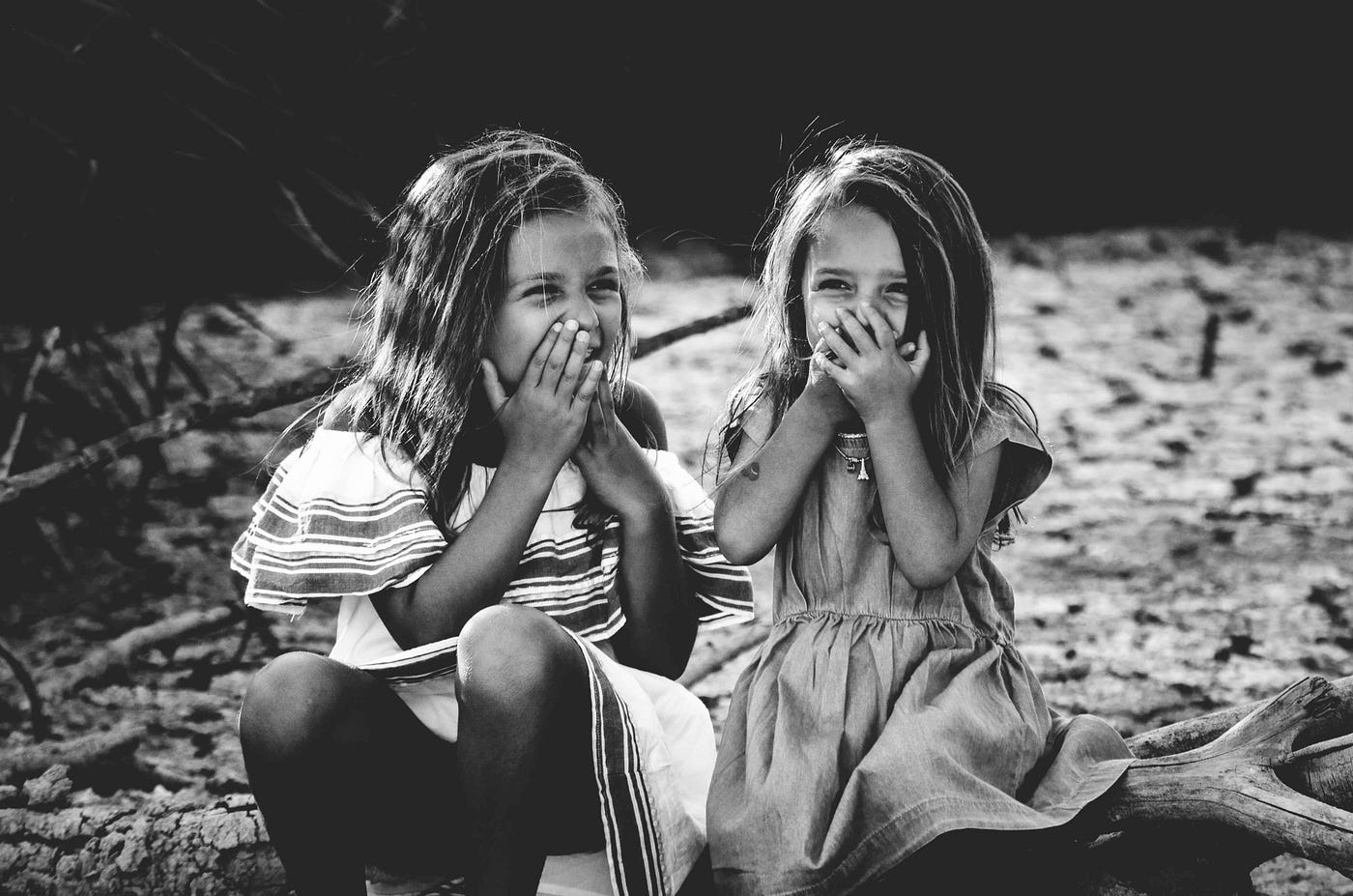 black & white photo of two young girls laughing with their hands over their mouths