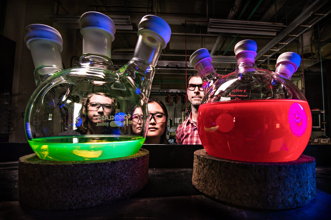 Four people sitting behind two glass tubes with colorful liquids