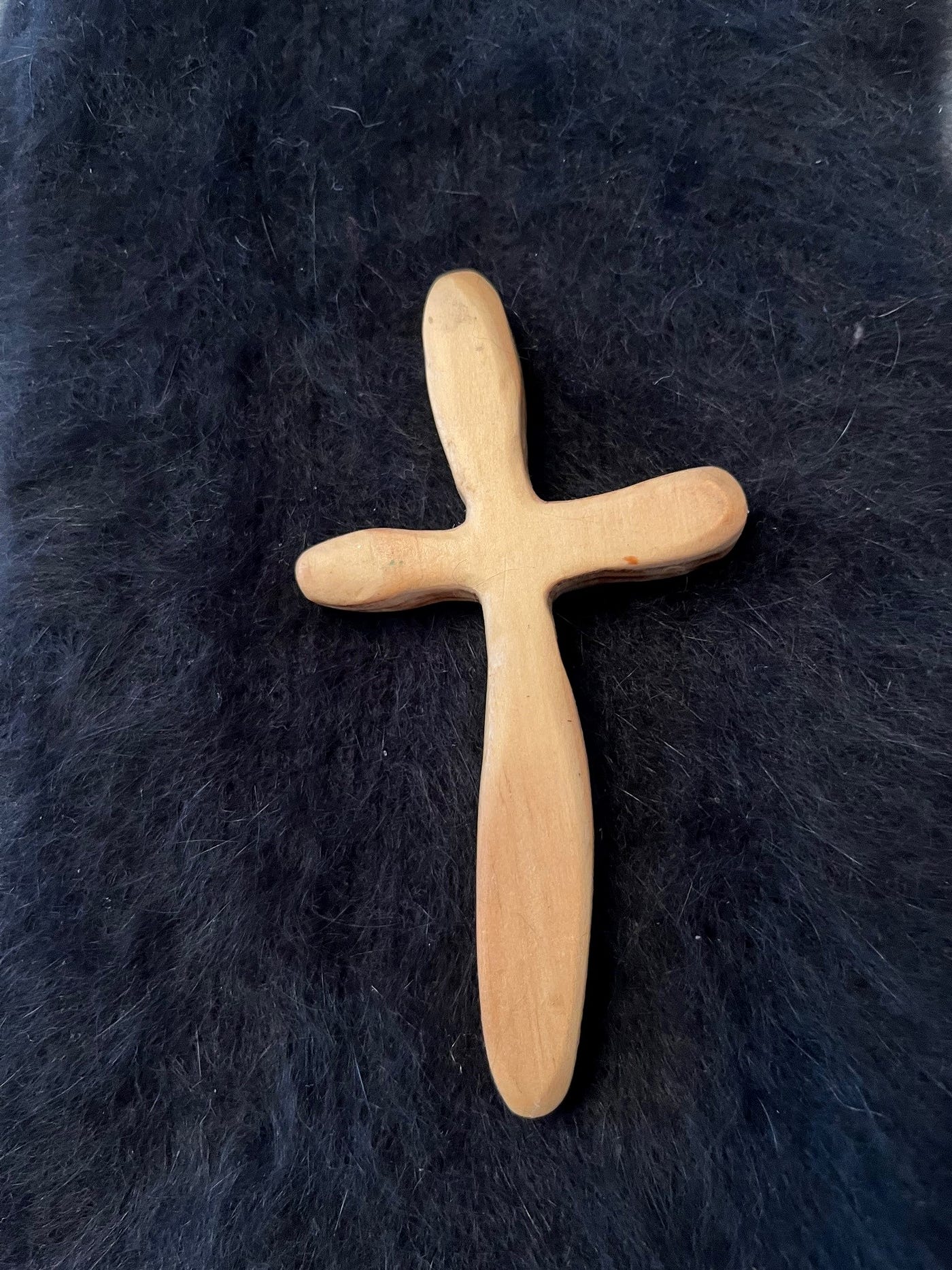 A slender, blond, wooden cross on a black angora rug.