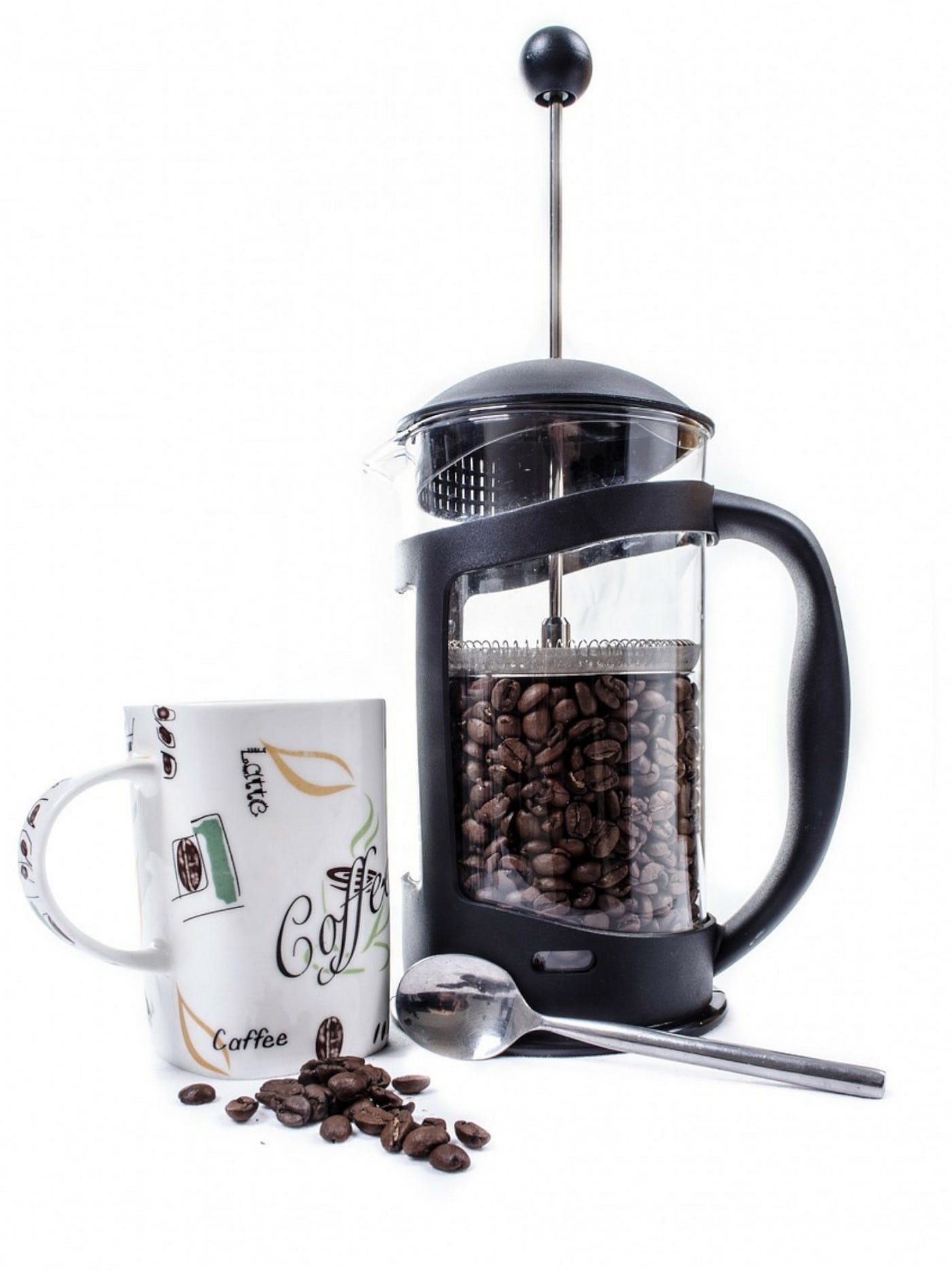 Color photo of a black colored French Press with coffee beans in it, a coffee cup and a spoon on the side.