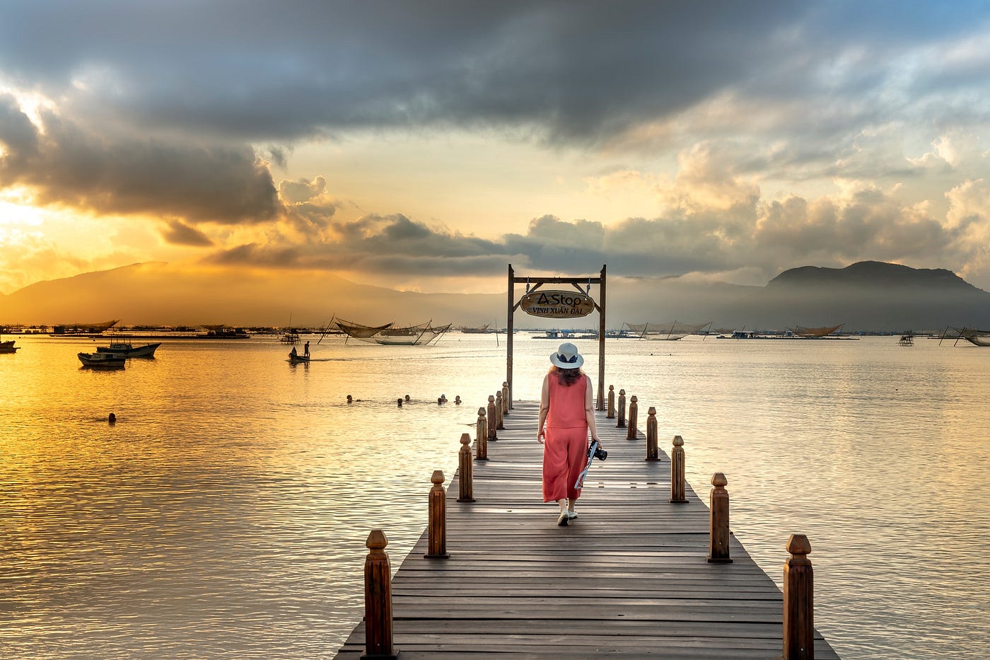 Back view of woman in pink outfit walking on dock during sunset