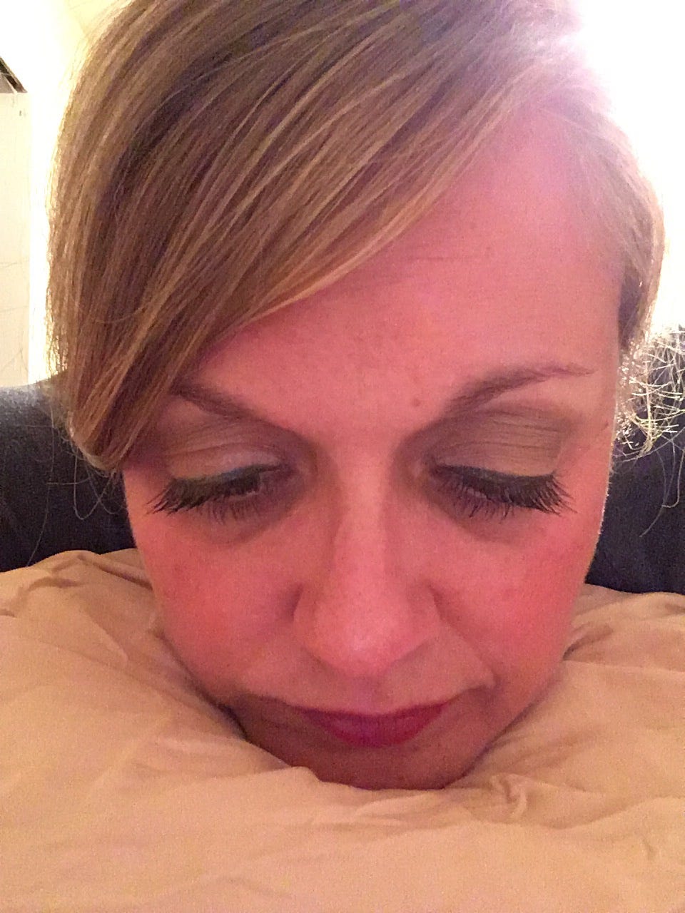 A downtrodden looking individual with head on pillow and eyes downcast.