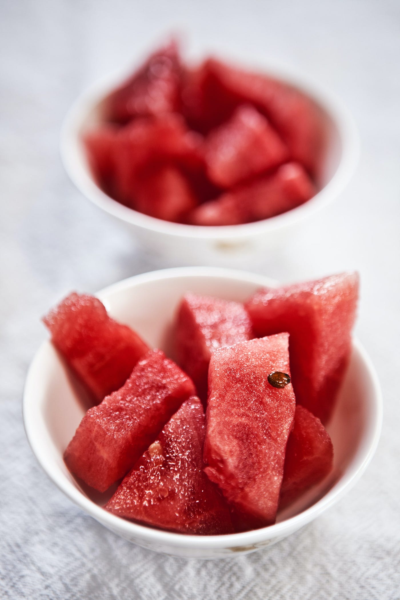 Two bowls of cut up watermelon on the counter.