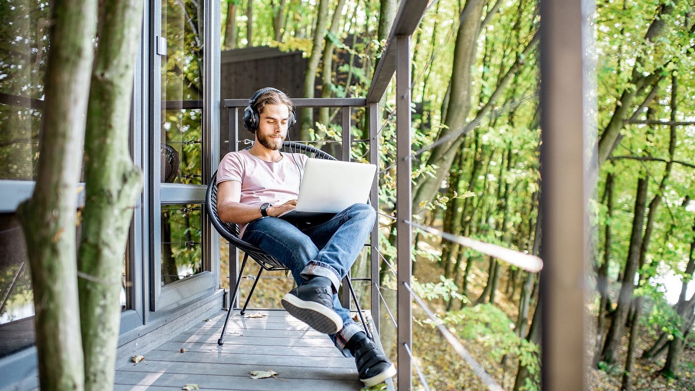 Man working on laptop on a porch in a cabin in the woods