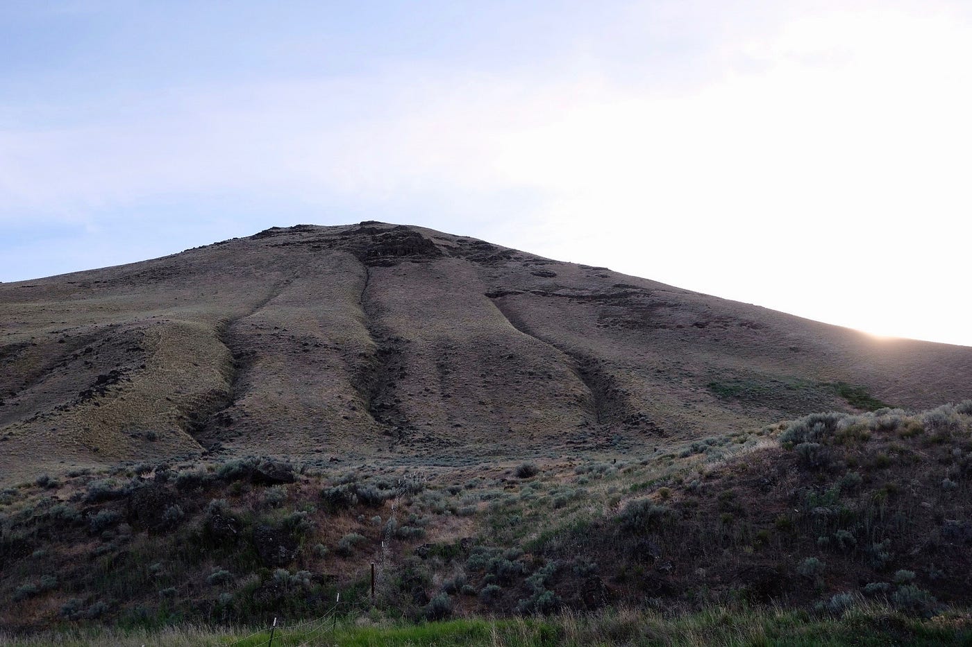 The sun sets behind a hill grooved with strange parallel lines.