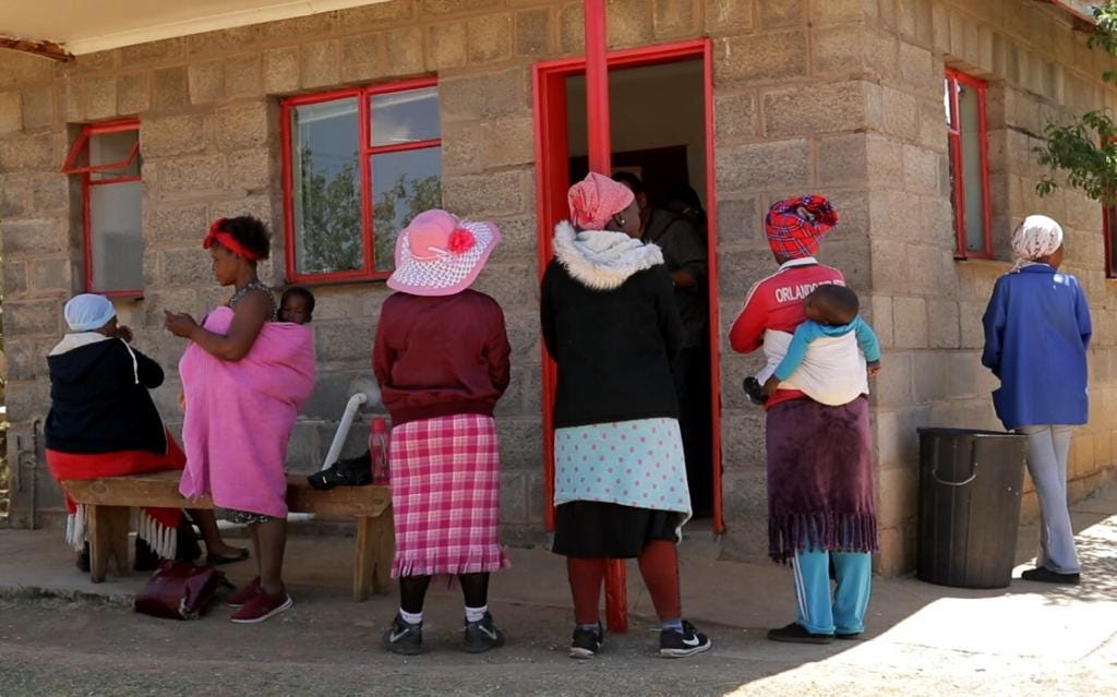 Women and babies waiting in a line outside a clinic.
