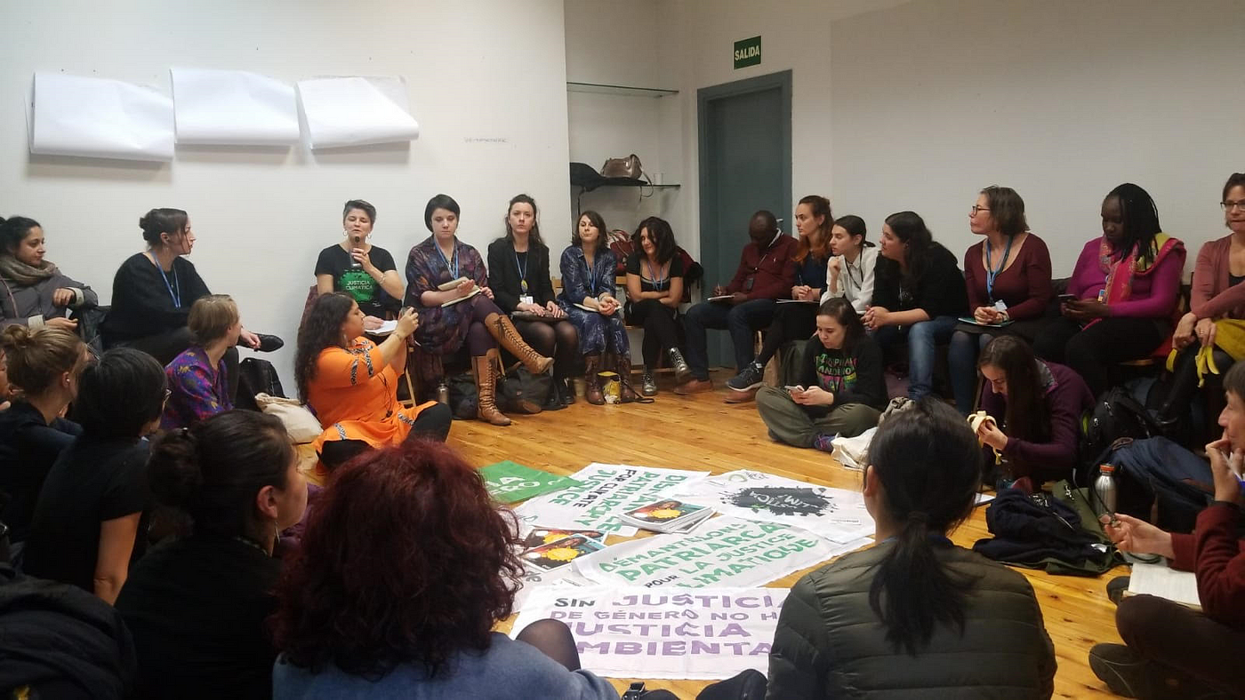 A group of people in a circle listening to speakers with rally signs in the middle of the circle on the floor