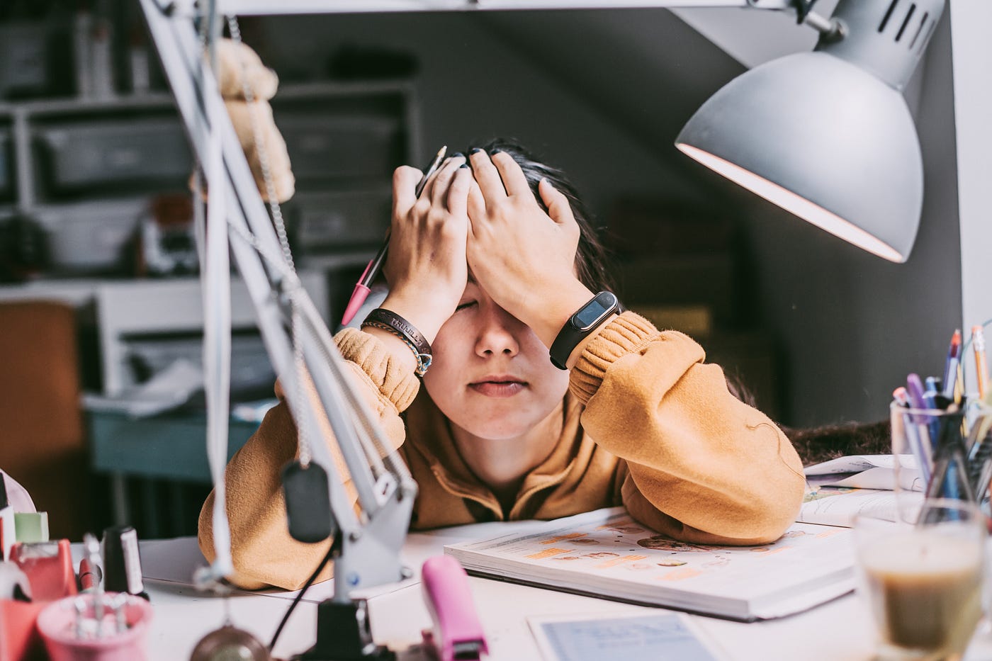 A person slumped at a desk, propping their hands up on their elbows, their hands on their forehead.