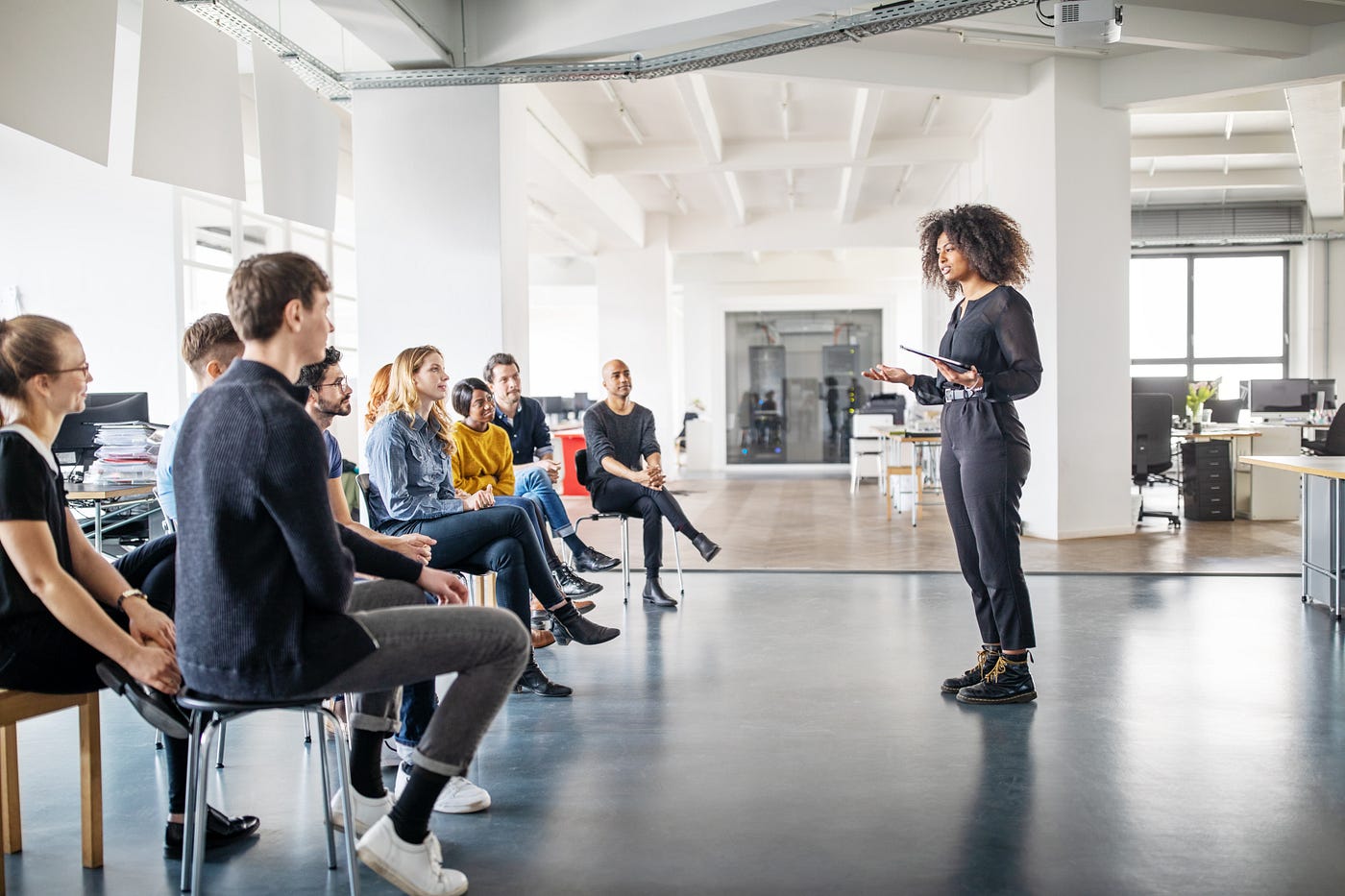 A young woman stands in front of her team and addresses them in a meeting.
