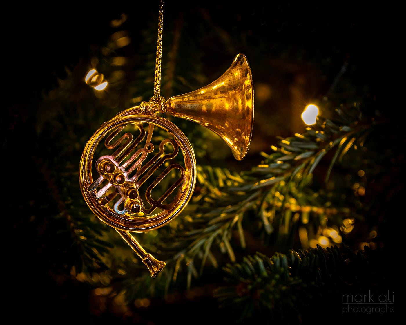A gold French horn ornament hangs from a branch of a Christmas tree.