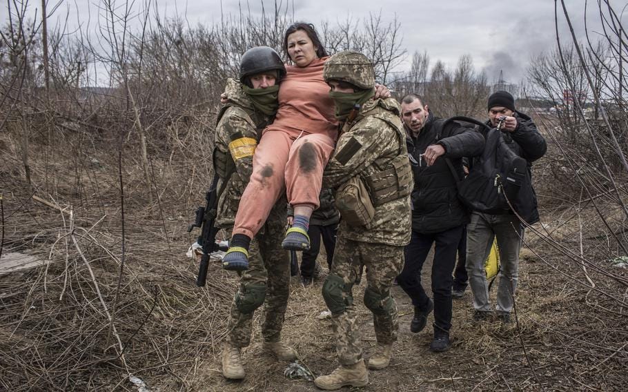 A woman carried by Ukrainian soldiers crosses an improvised path while fleeing the town of Irpin, Ukraine, Sunday, March 6, 2022. In Irpin, near Kyiv, a sea of people on foot and even in wheelbarrows trudged over the remains of a destroyed bridge to cross a river and leave the city. (Oleksandr Ratushniak/AP)