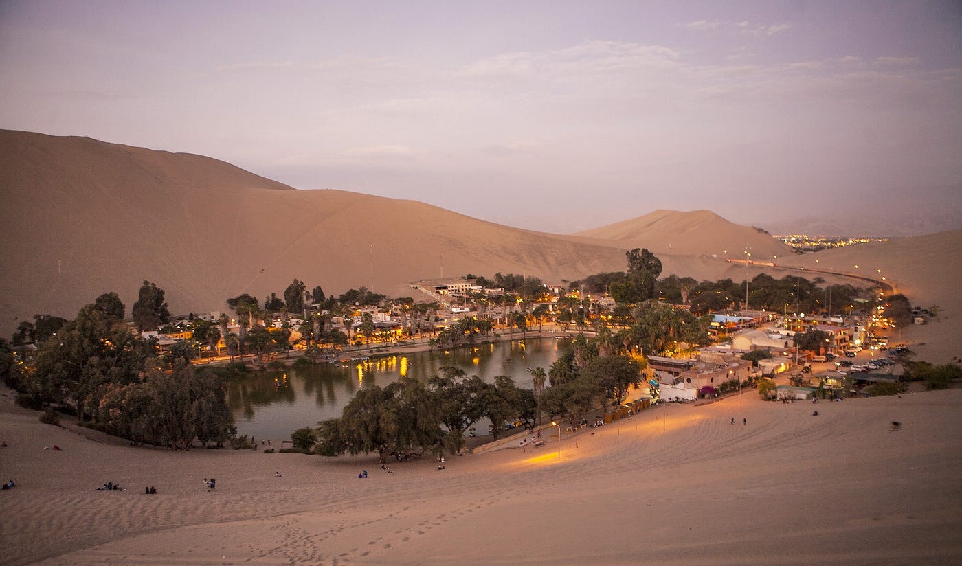a lovely little oasis town, surrounding a small body of water, at dusk, looking lively and comfortable in an otherwise very barren desert.