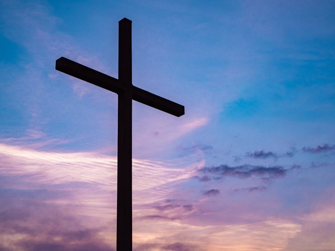 A picture of a cross against a blue and pink sky.