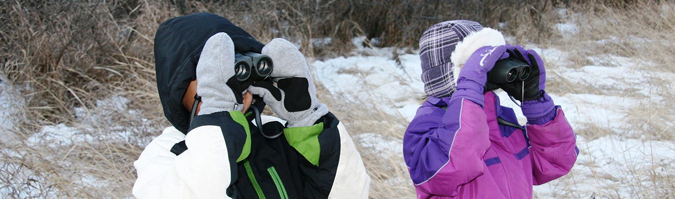 Kid wearing jackets and mittens and looking through binoculars.