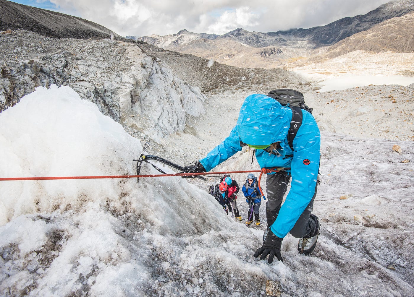 person climbs a mountain, while friends watch and cheer them on below.
