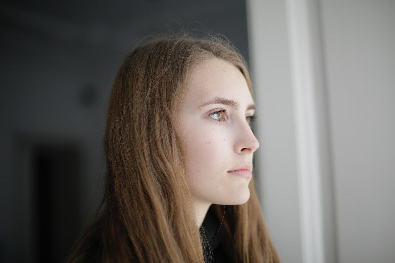 Pensive young woman looking out window. Never accept an incomplete or inauthentic apology