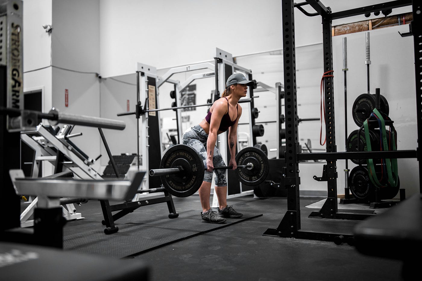 A woman is in the middle of a heavy deadlift. She is in an empty gym, focused and wearing a cute baseball cap.