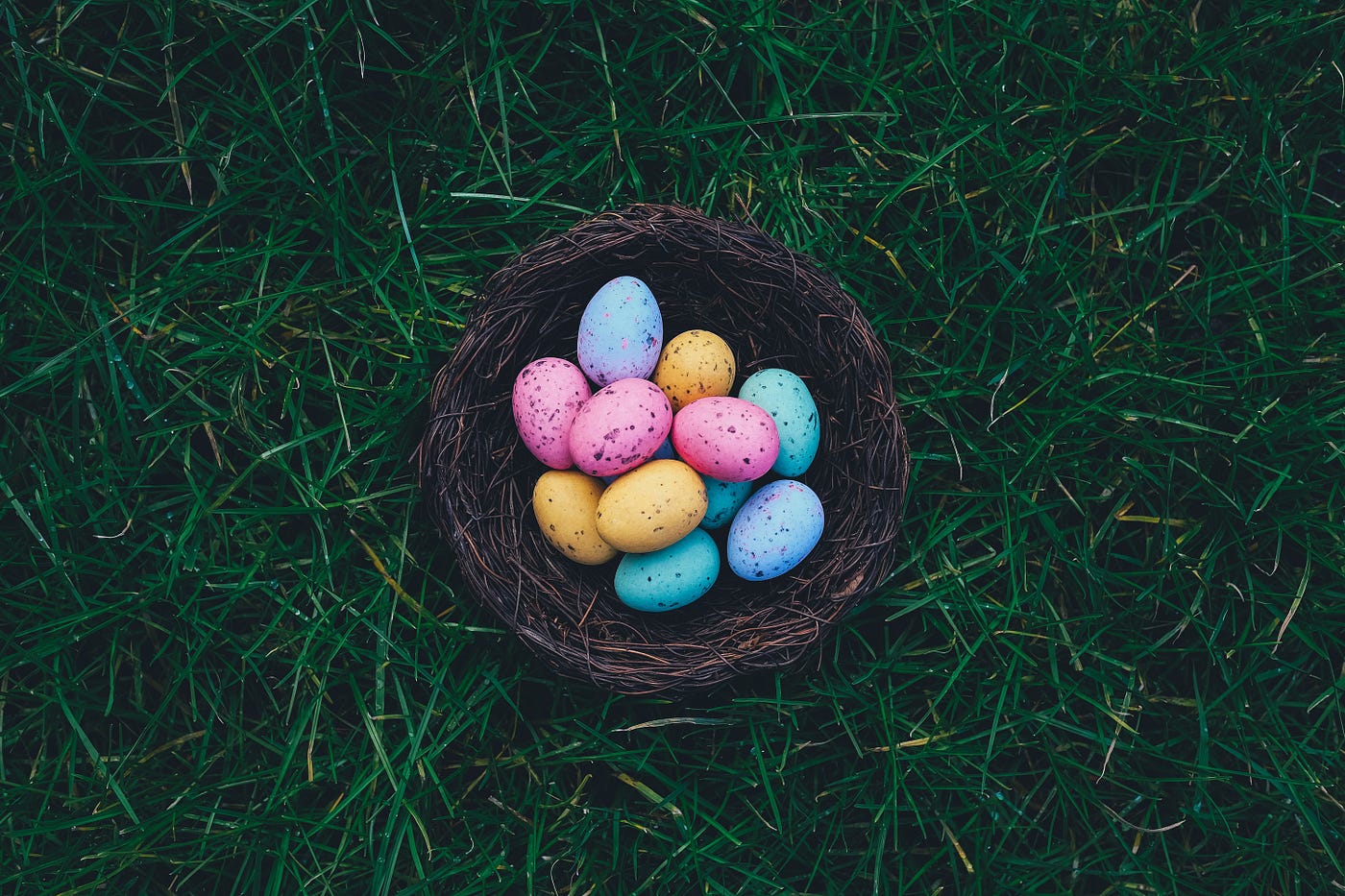 colorfully assorted easter eggs against brown basket on grass