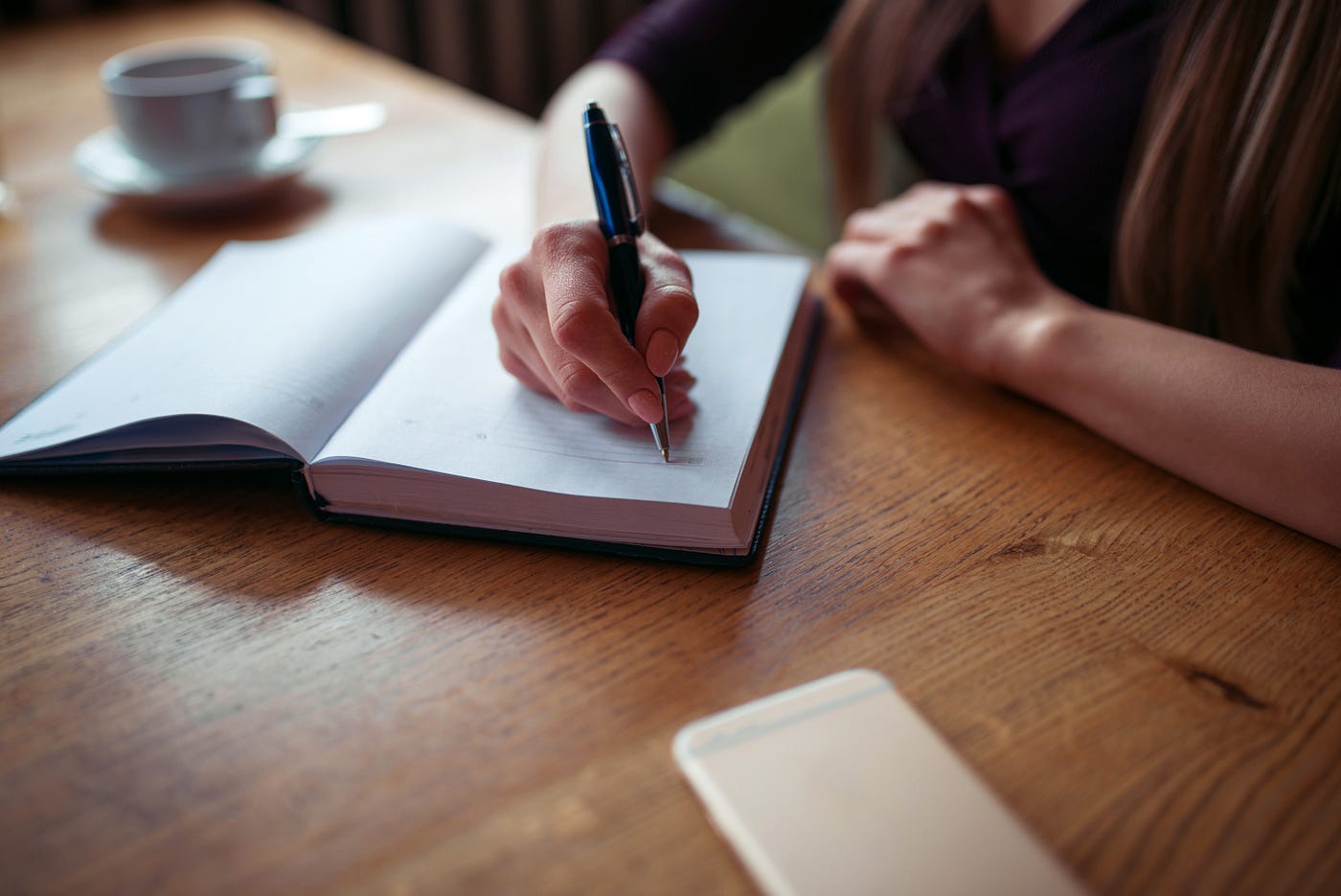 Person writing by hand with a coffee cup at a table