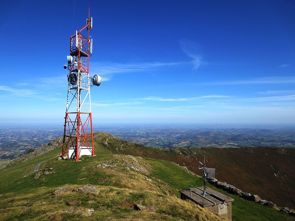 The image shows an antenna at the summit of Baigura with Labourd in the French Basque Country in the background.