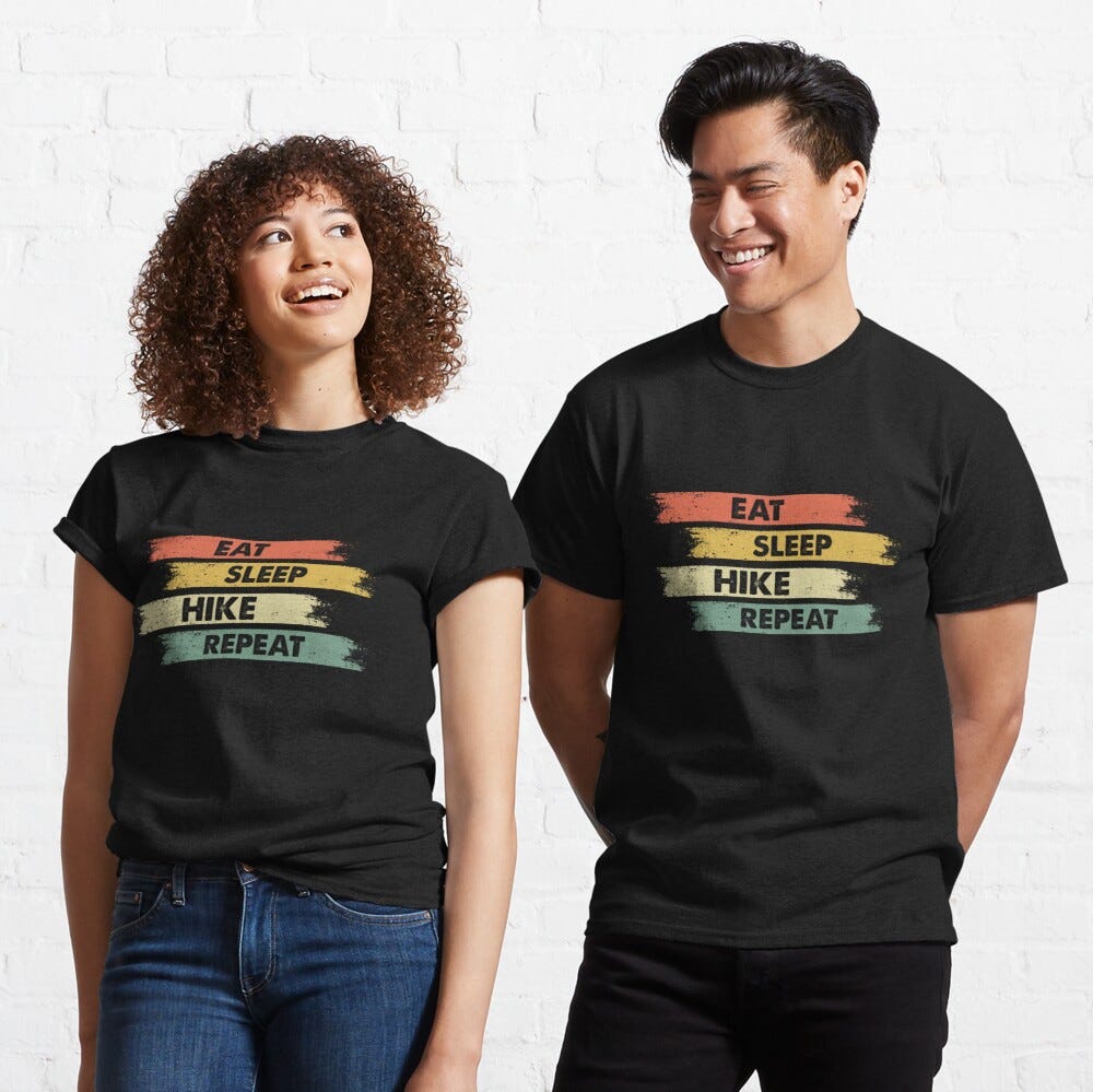 Man and Woman Wearing a black classic t-shirt with amazing illustration and text saying “eat sleep hike repeat”.