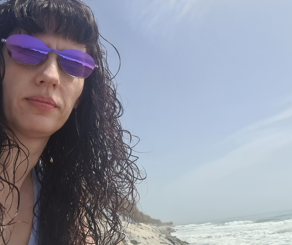Alice with sunglasses and the beach behind her