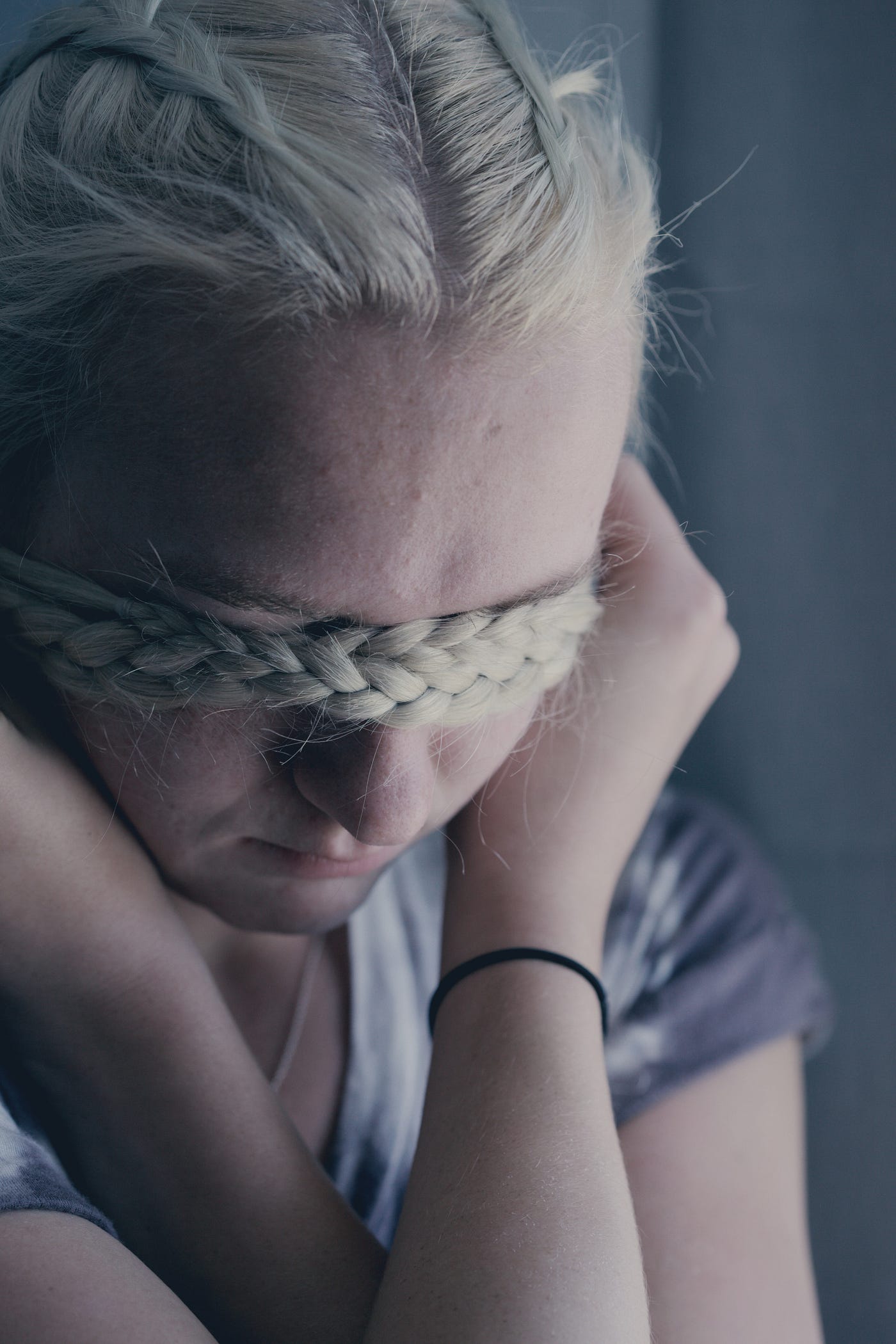 Blonde white womxn uses her own french braids to cover her eyes