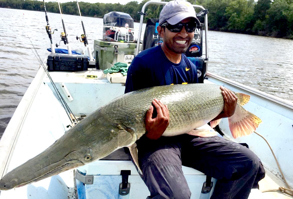 man holds a large gar on a boat