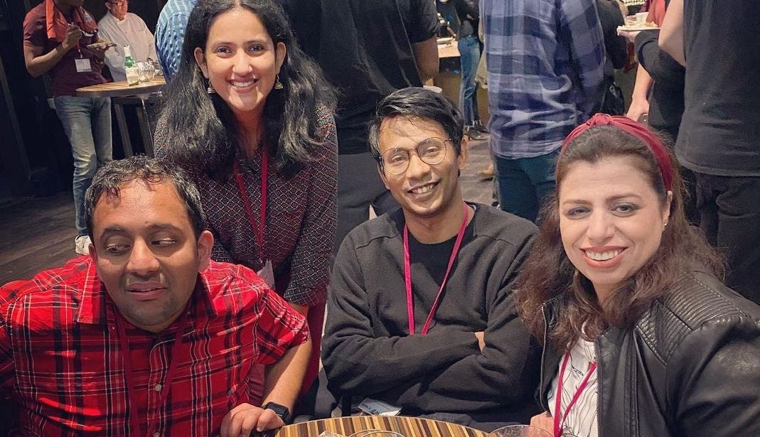 A group of four people smiling in a casual setting. Ather is in the center, his arms crossed amiably.