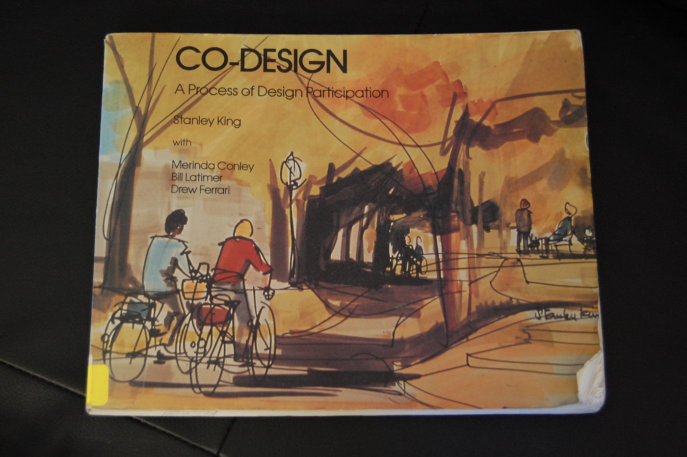 A picture of book that is golden in colour with illustration on it of two people cycling on bikes. The title says Co-Design