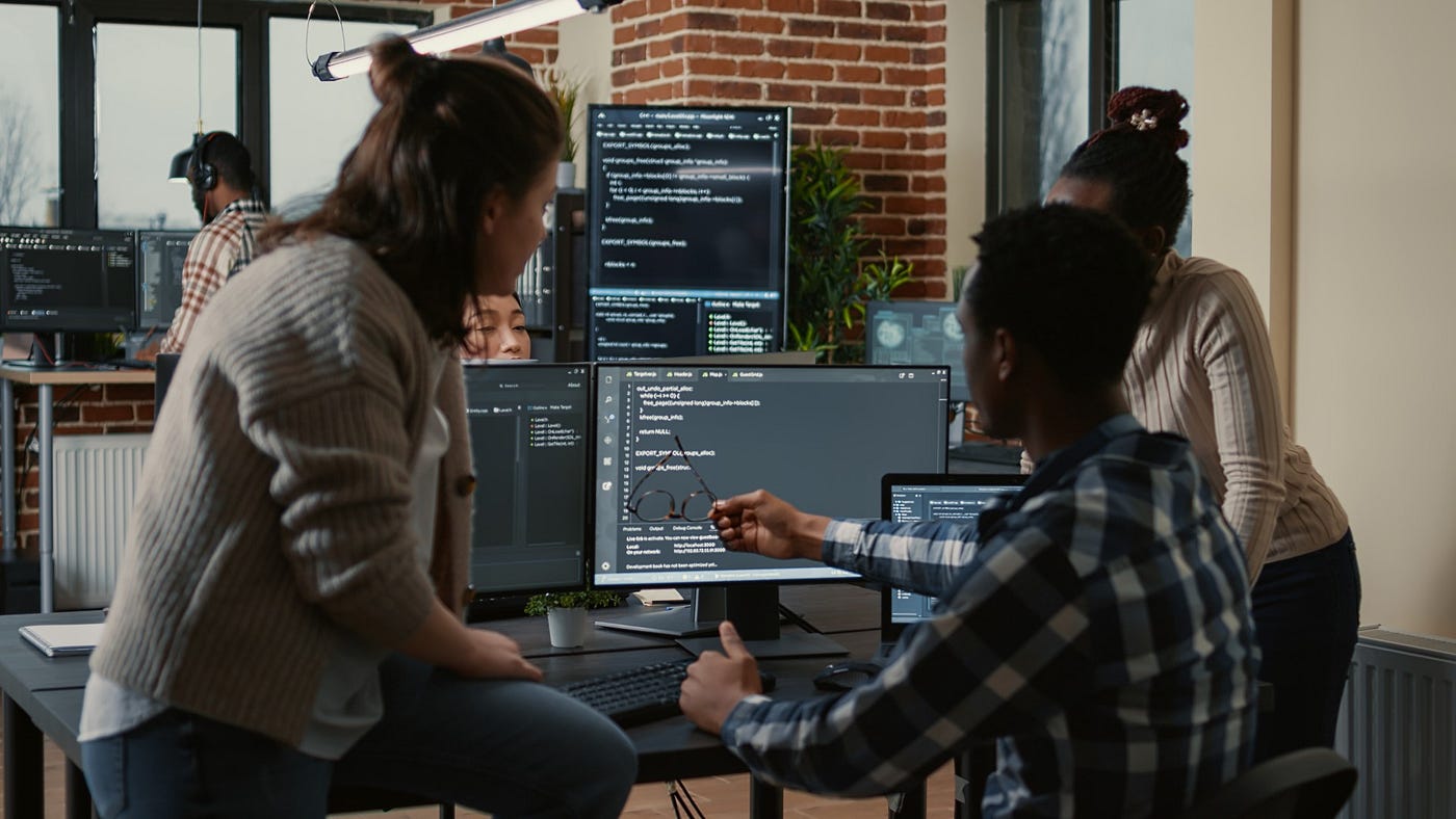 Three individuals looking at some code on a computer screen.