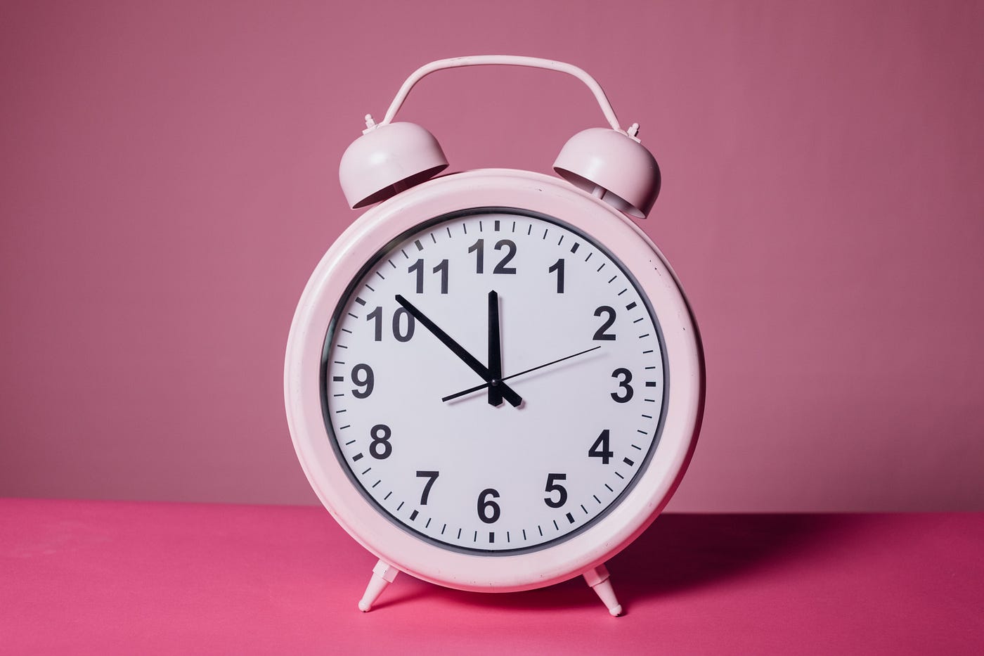 A pink clock in front of a pink background.
