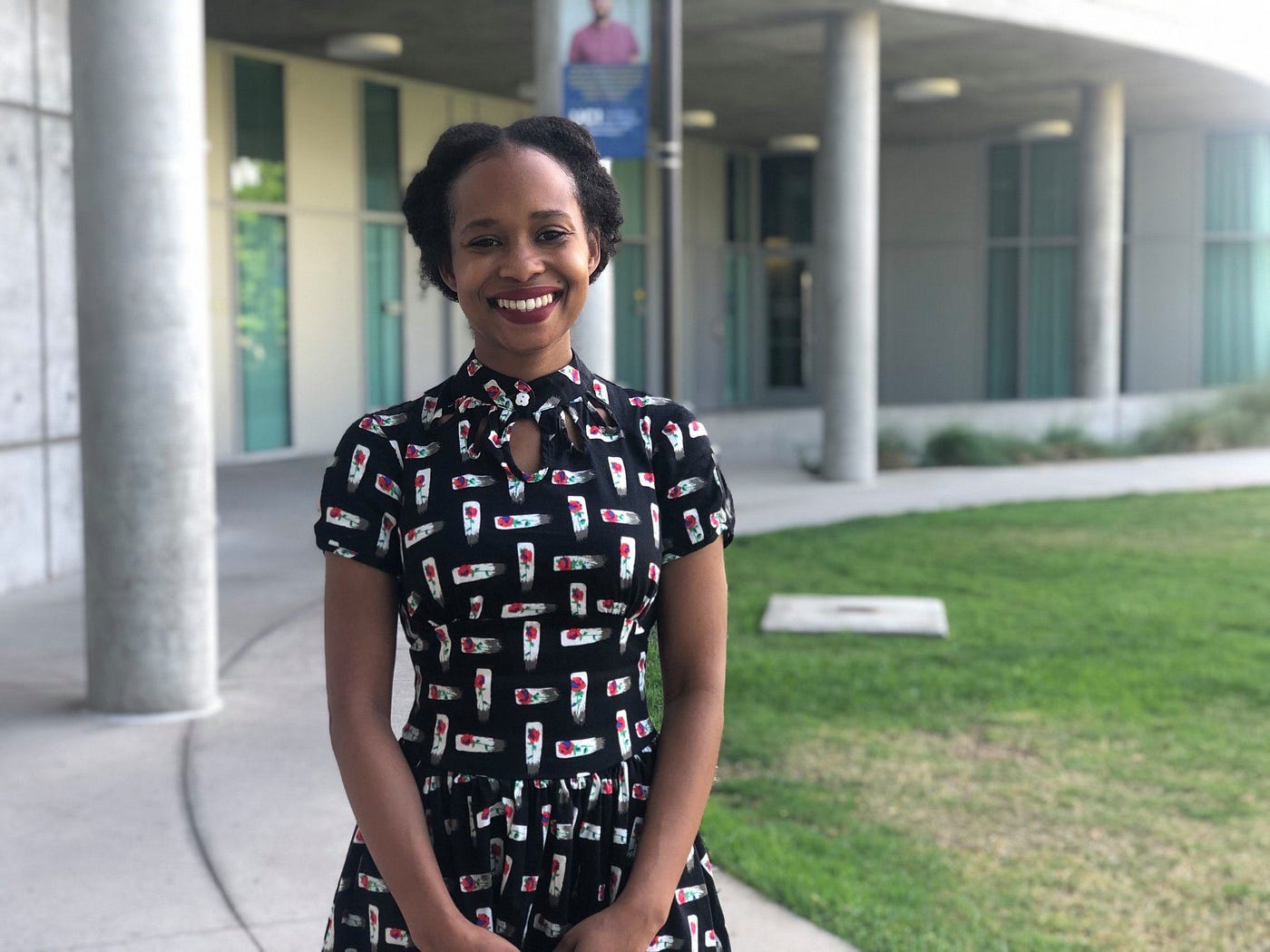 Brittnay Proctor stands outside of Humanities Gateway smiling and holding her hands in front of her.
