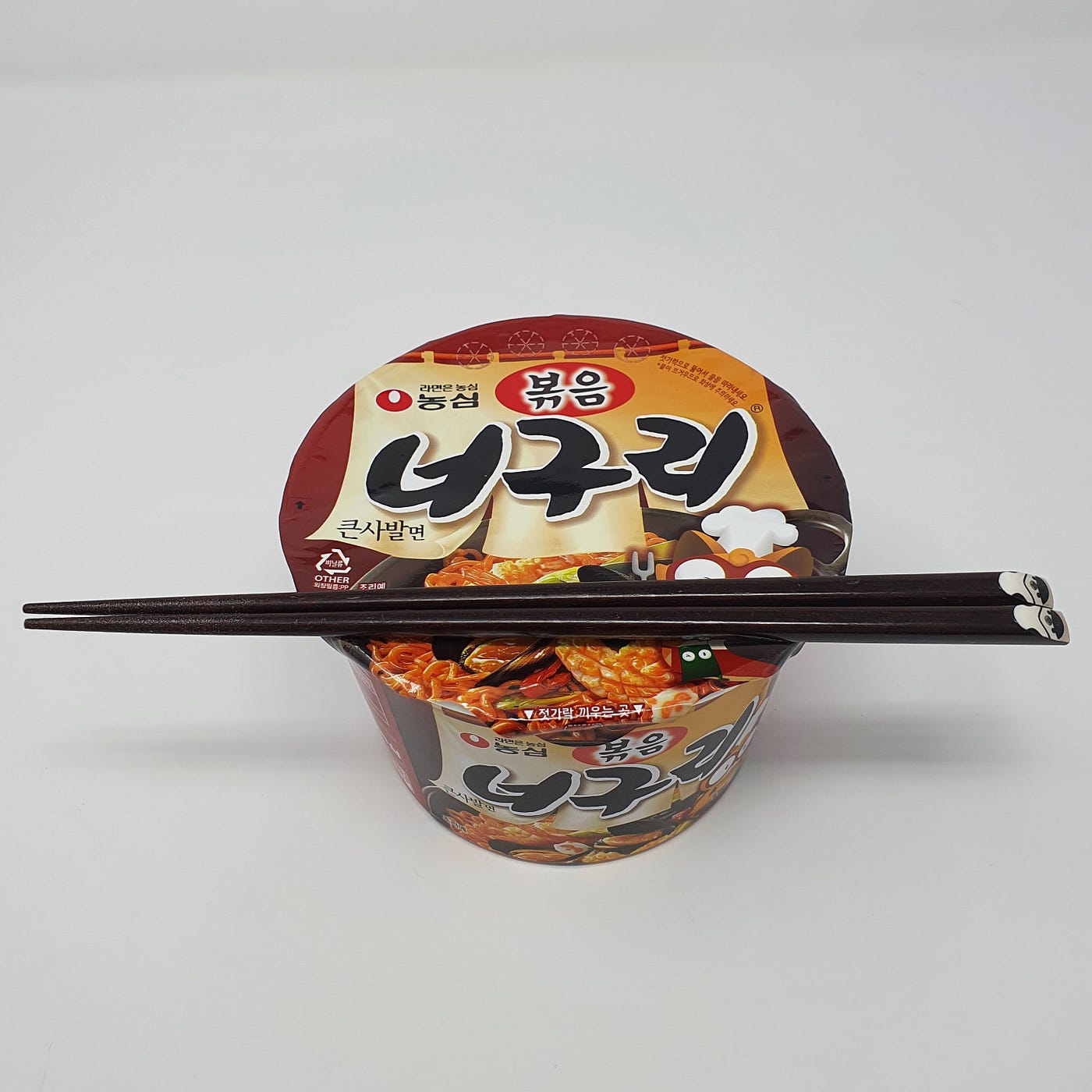 A closed cup of Nongshim Bokkeum Neoguri Instant Noodles cooking for 4 minutes with chopsticks resting on top.