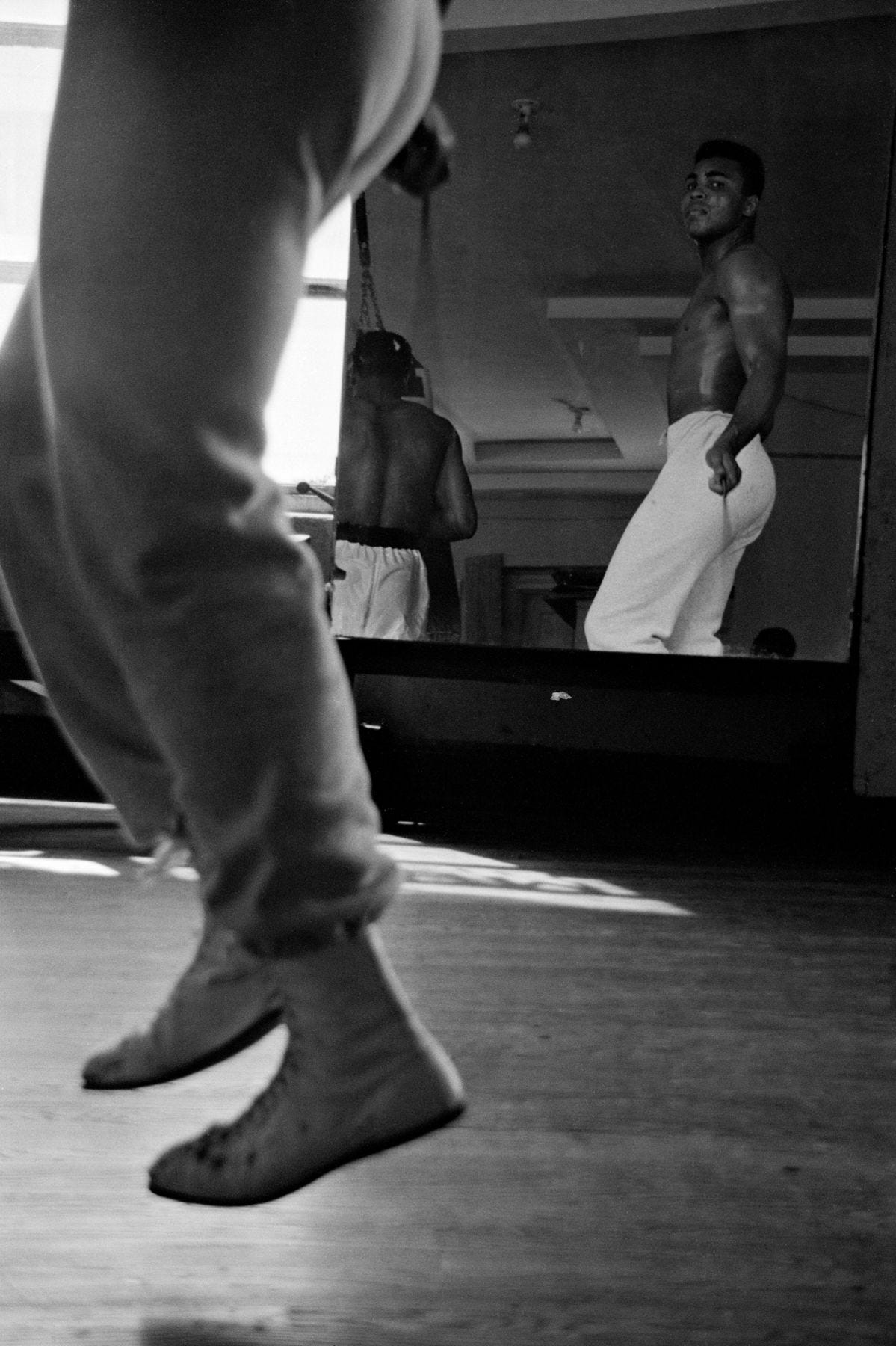 Young Muhammad Ali looking in at his reflection in a mirror as he is skipping rope in a gym