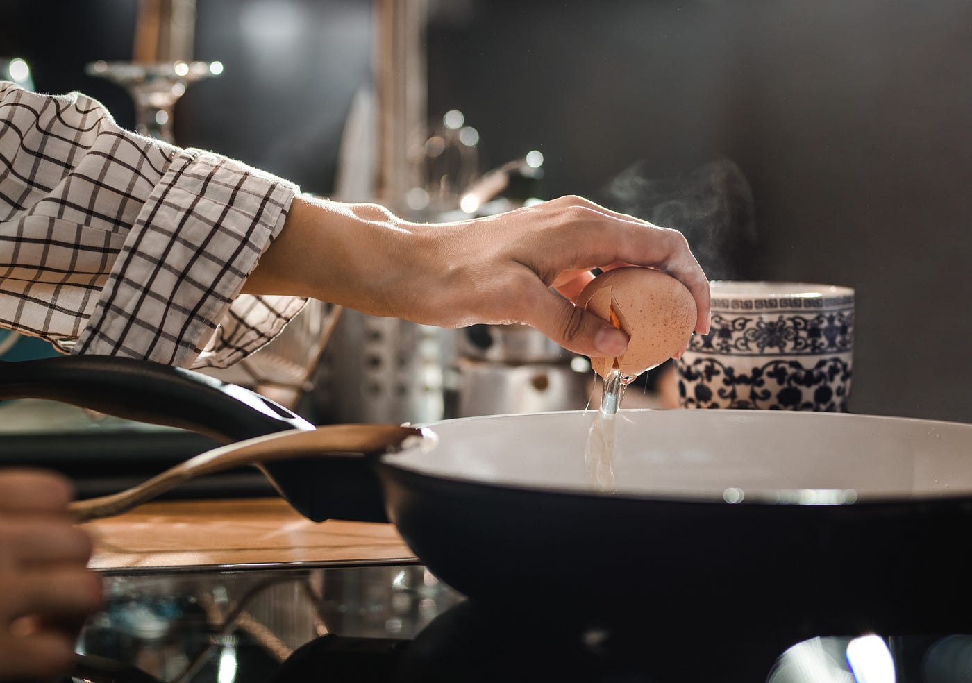 Close up of unrecognizable woman cracking an egg for breakfast while putting it in a frying pan.