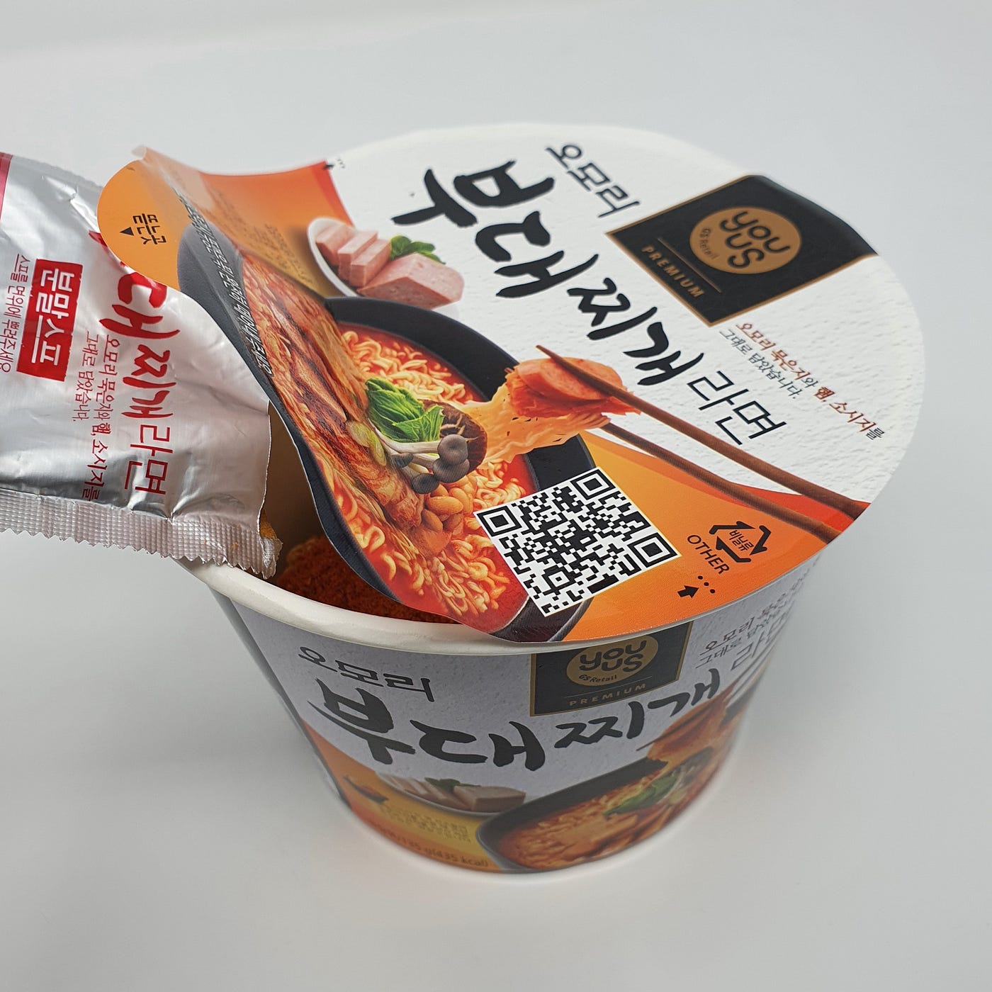 Adding the powdered soup packet to a cup of YouUs Omori Budae-jjigae Ramen.