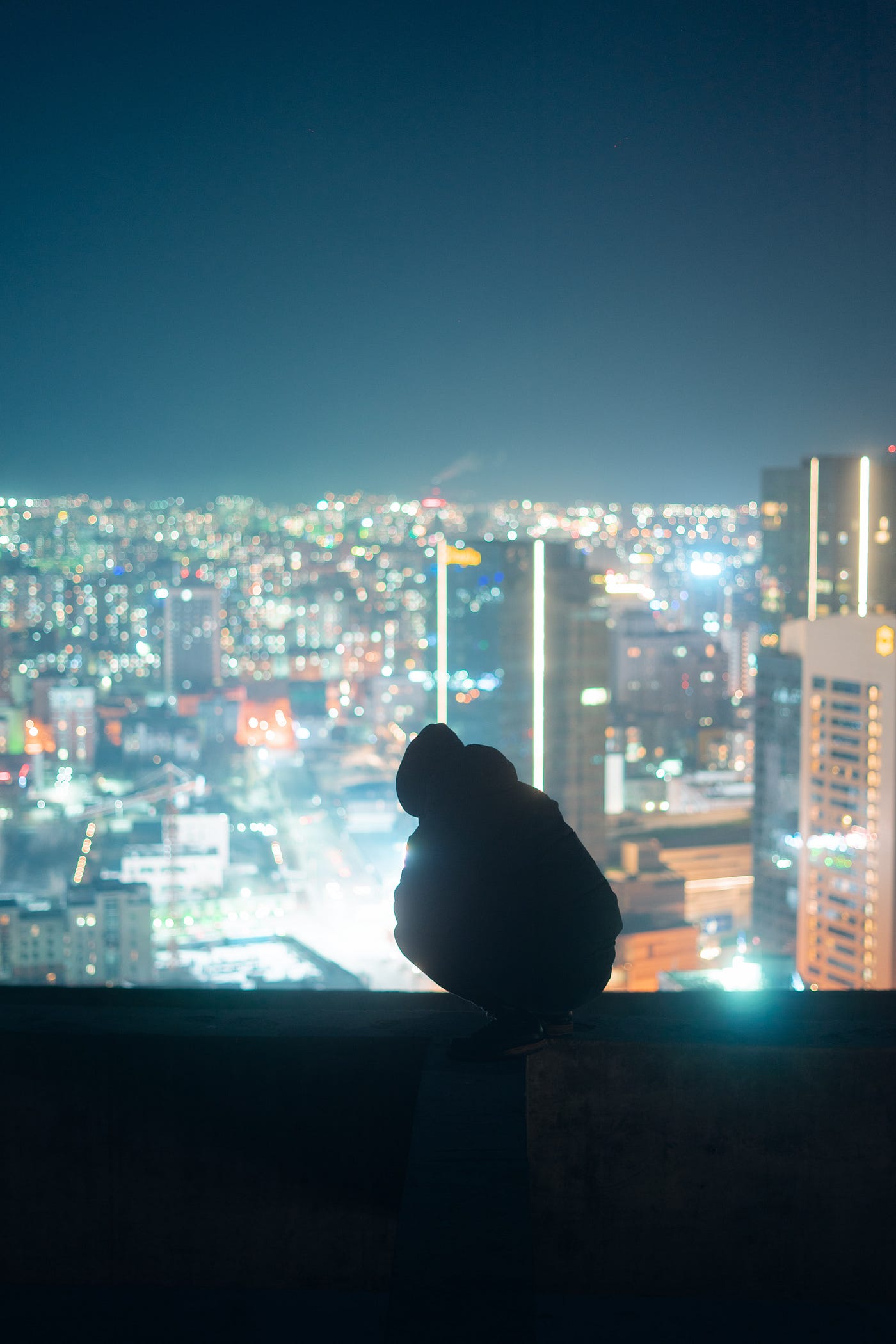A person on a rooftop looking down to the night city