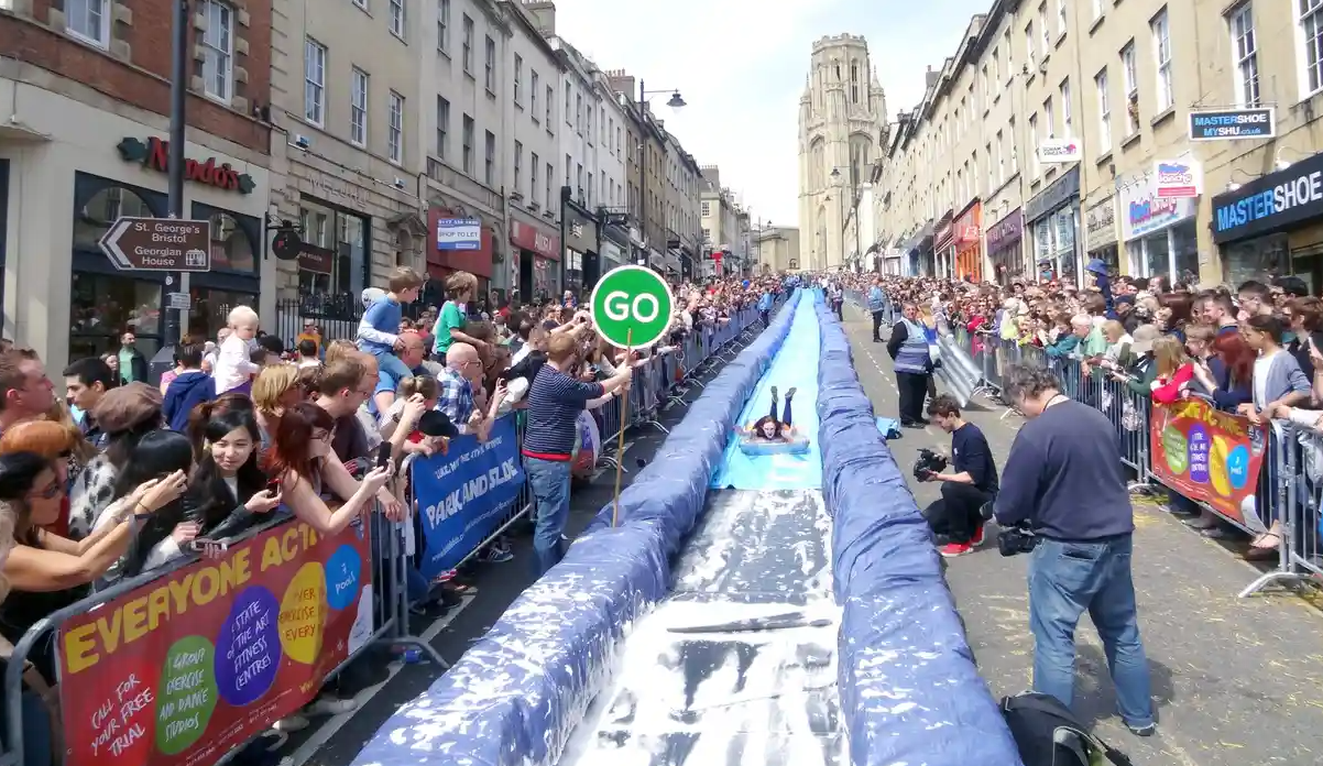 Girl slides down a water slide in the middle of the city around a crowd