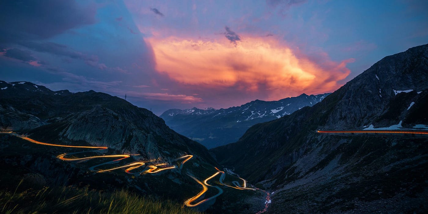 Sunset behind a mountain with a lit up winding road heading down the mountain