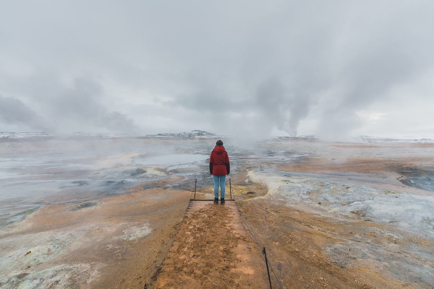 A photo of a person standing, back to the camera, in a desolate landscape. It is gloomy and looks cold.