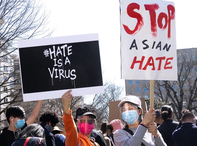 Two protestors hold up signs that read “#hate is a virus” and “stop Asian hate”