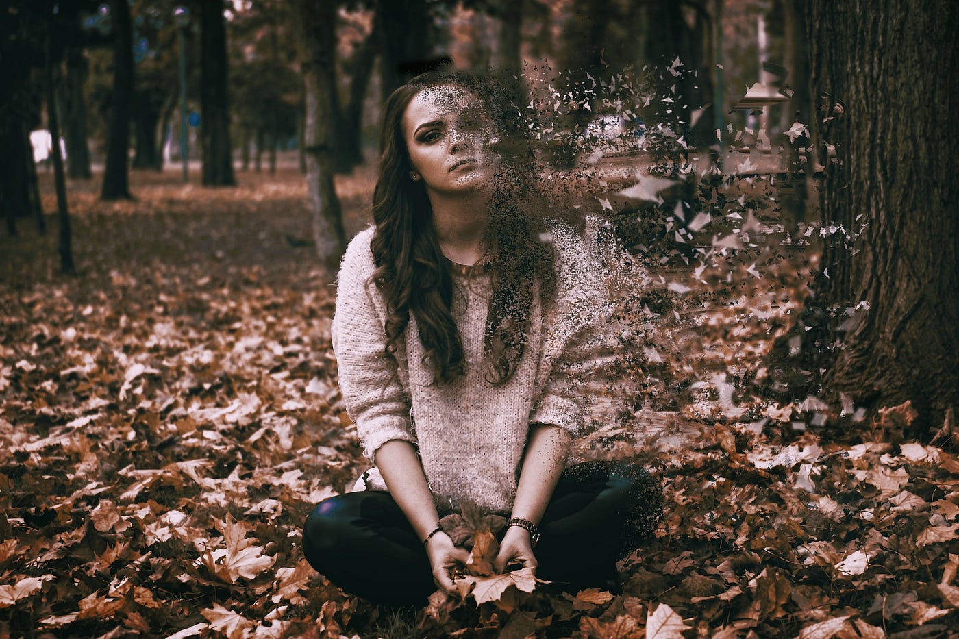 Sad girl sitting on a pile of leaves in the woods
