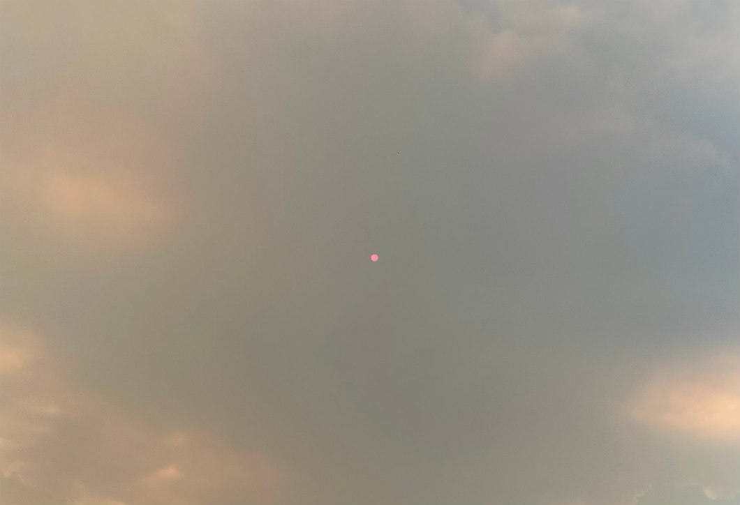 Sky thick with what looks like clouds but is actually a smoke plume from a forest fire. A small red shiny dot is visible in the center of the photo, which is the sun.