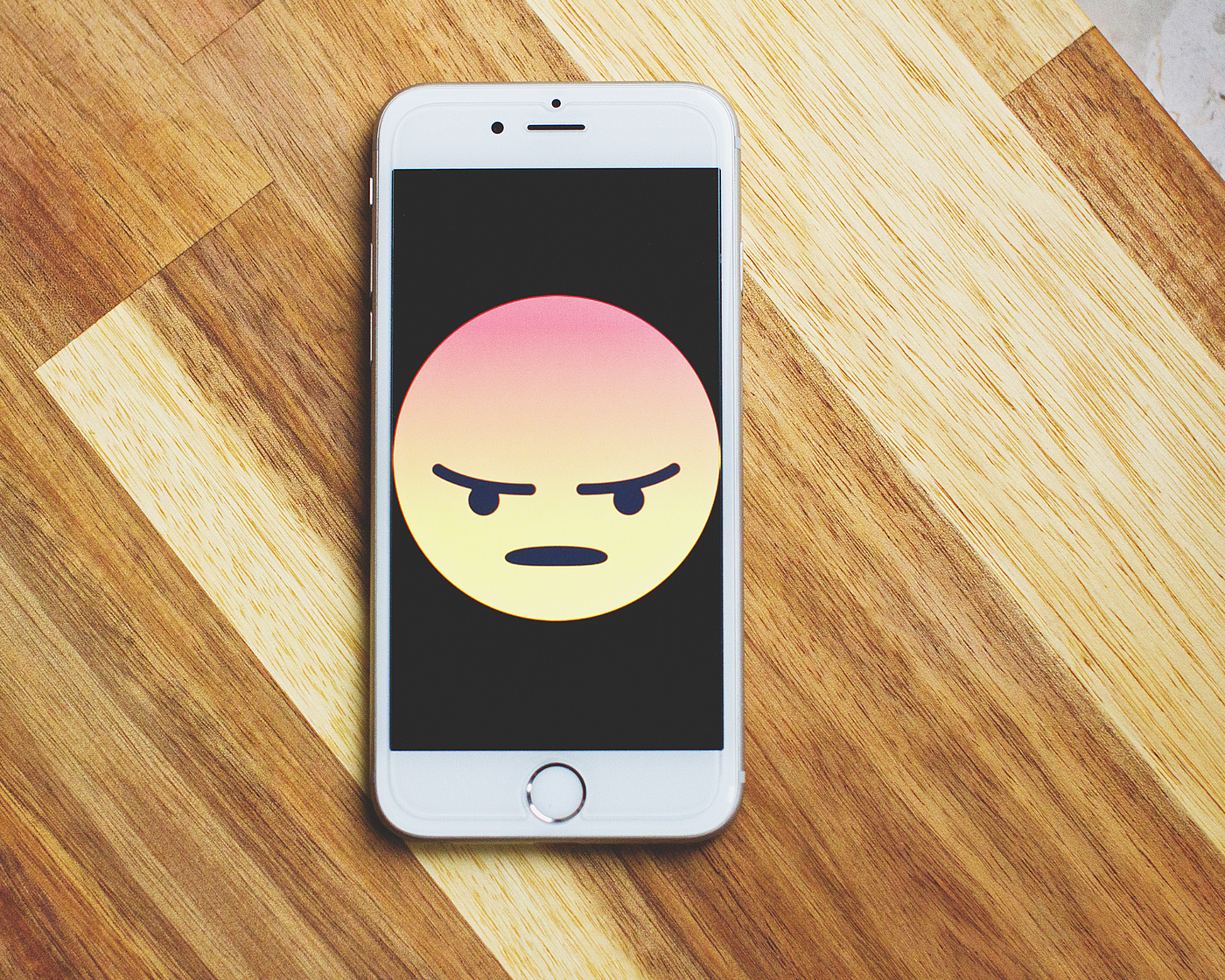 A phone with a full screen angry face emoji